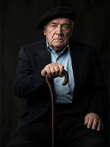 Retrato pictórico editado de hombre mayor con boina y bastón con tonos cálidos y alto contraste estilizado