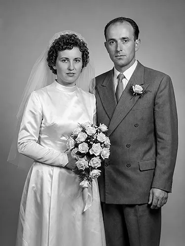 Retrato de boda en blanco y negro restaurado con la novia sosteniendo un ramo de rosas junto a su esposo
