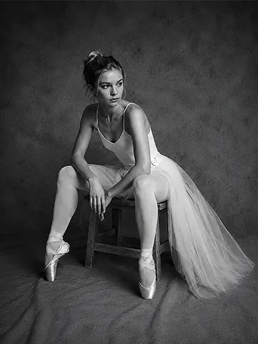 Fotografía en blanco y negro de una bailarina de ballet sentada con falda de tul y zapatillas de punta.