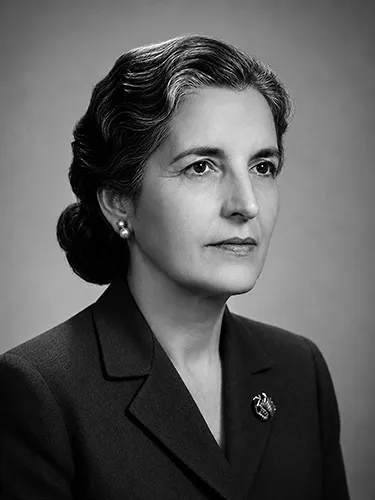 Retrato en blanco y negro restaurado de una mujer con traje oscuro, pendientes de perlas y broche.