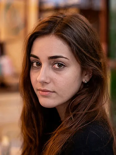 Retrato enfocado de una mujer joven con un pequeño lunar en la mejilla y pendientes discretos.