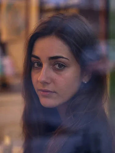 Retrato de una mujer joven con cabello oscuro mirando fijamente a través de un cristal con reflejos.