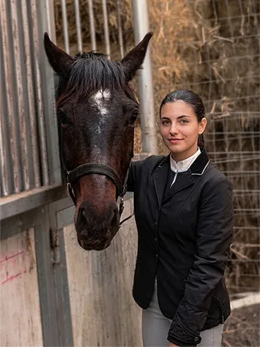 Joven amazona sonriente junto a su caballo en las cuadras.